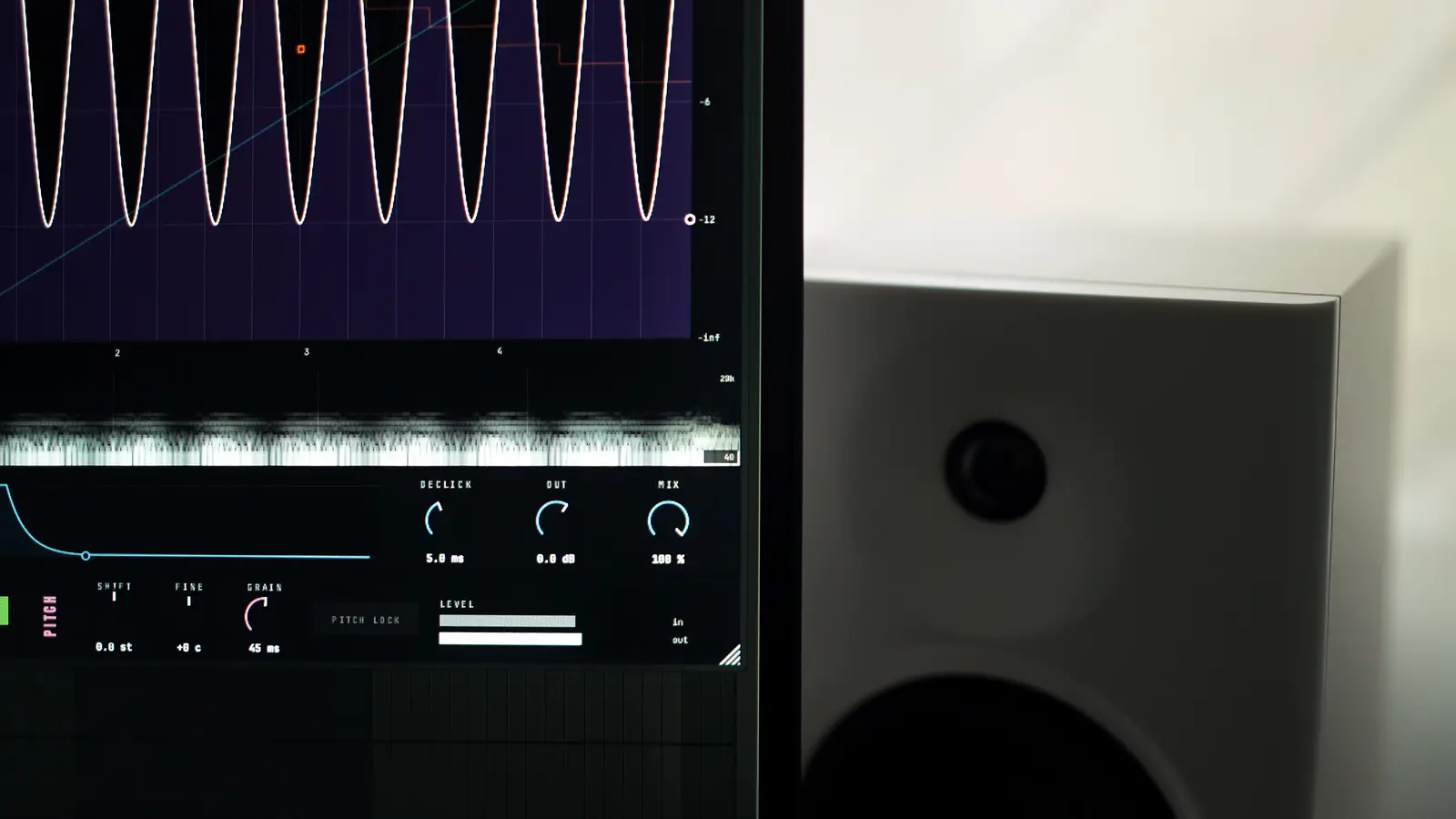 A monitor filling most of the frame with the Lapse window open on it, the volume lane drawn as a row of steep dips and the spectrum running underneath. A white studio monitor stands beside the screen.